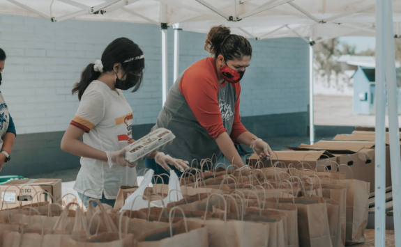 People help at a pop-up food bank packing bags with goods. They are wearing face masks.